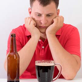 грустный мужчина сидит перед кружкой пива